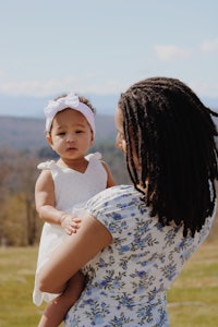 a woman holding a baby in a field with mountains in the background