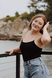 a young woman posing for a photo on a railing near the water