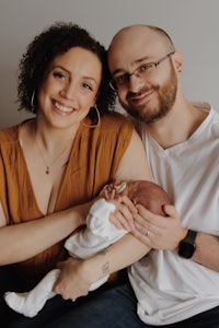 a man and woman are holding a baby in front of a gray background