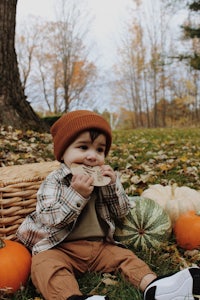 a baby sitting on the ground with pumpkins in the background