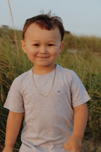 a young boy in a gray t - shirt standing in tall grass