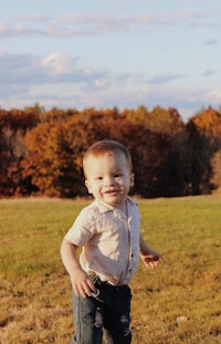 a baby boy is standing in a field with trees in the background