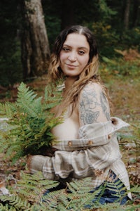 a woman holding a bunch of ferns in the woods