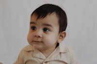 a baby in a tan shirt sitting on a white background