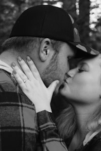 black and white photo of a couple kissing in the woods