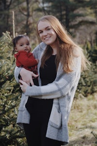 a woman holding a baby in front of a christmas tree farm