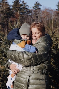 a woman holding a child in front of a christmas tree farm