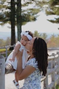 a woman kisses her baby in front of a fence