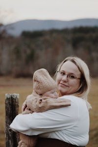 a woman holding a baby in front of a fence