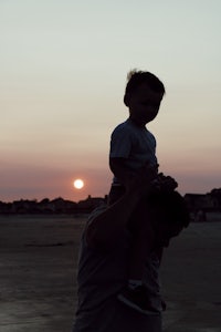 a man holding a child on his shoulders at sunset