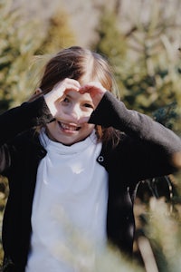 a little girl making a heart with her hands in a christmas tree field