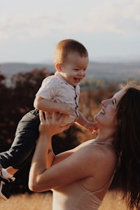 a woman holding a baby in the air in a field