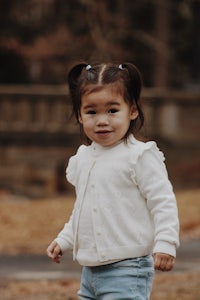 a little girl wearing a white cardigan and jeans