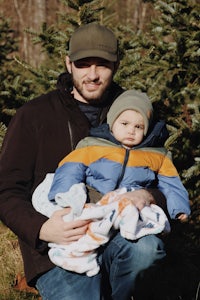 a man holding a baby in front of a christmas tree farm