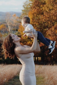 a woman is holding her baby in the air in a field