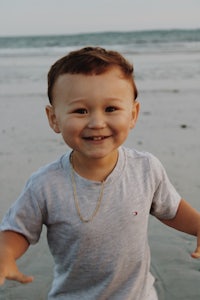 a young boy standing on the beach with a necklace