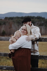 a man and woman hugging a baby in a field