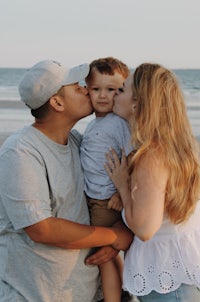 a man and woman kissing their son on the beach