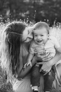 a black and white photo of a woman holding a baby in a field