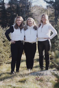 three women posing in front of a christmas tree farm