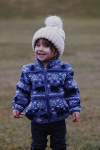 a little girl in a blue jacket and hat standing in a field