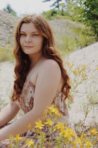 a girl in a dress sitting in a field of yellow flowers