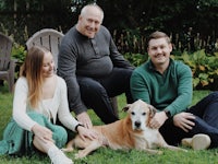 three people sitting on the grass with a dog