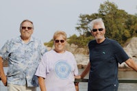 three people standing on a railing next to a body of water