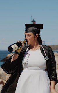 a woman in a graduation gown drinking a bottle of wine