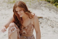 a woman in a tan dress sitting on the sand