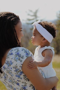 a woman holding her baby in a field with mountains in the background