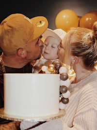 a man and woman kissing a baby in front of a cake