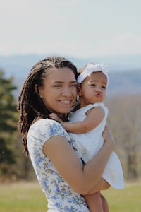 a woman with dreadlocks holding a baby in a field