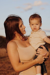 a woman holding a baby in a field