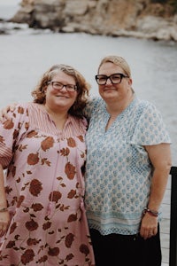 two women posing for a photo in front of a body of water