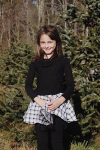 a little girl standing in front of a christmas tree farm