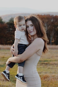 a woman holding a baby in a field with mountains in the background