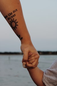 a woman holding a child's hand with a sun tattoo