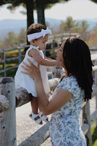 a woman holding a baby in front of a fence