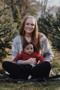 a woman holding a baby in front of a christmas tree farm