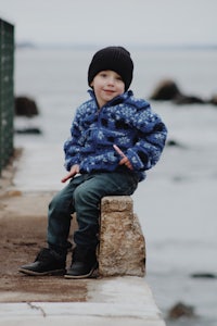 a young boy sitting on a ledge near the water