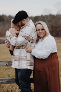 a man and woman hugging their baby in a field