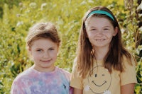 two girls standing in a field with smiles on their faces