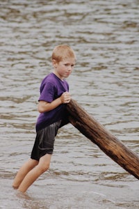 a young boy holding a log in the water