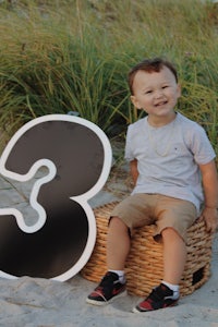 a young boy sitting on a wicker basket with a number three