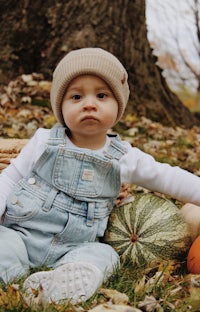 a baby in overalls sits on the ground next to pumpkins