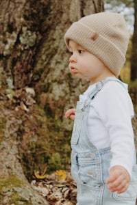 a baby wearing overalls and a beanie in the woods