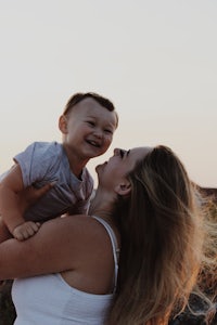 a woman is holding her son in the air at sunset