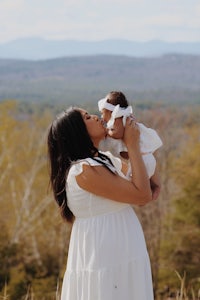 a woman kissing her baby in a field with mountains in the background