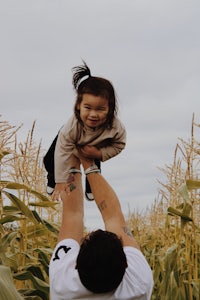 a man is holding a child in the air in a corn field